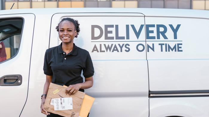A woman stands in front of a white van with a parcel.