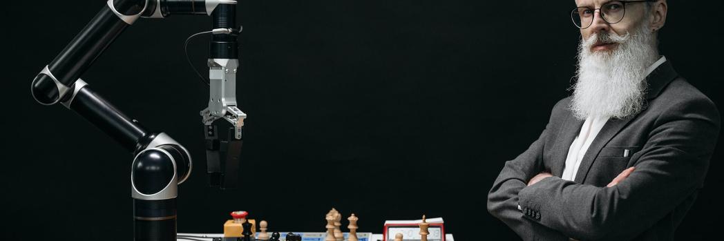 Älterer Mann mit grauen Haaren steht in einem Labor und spielt Schach gegen Künstliche Intelligenz