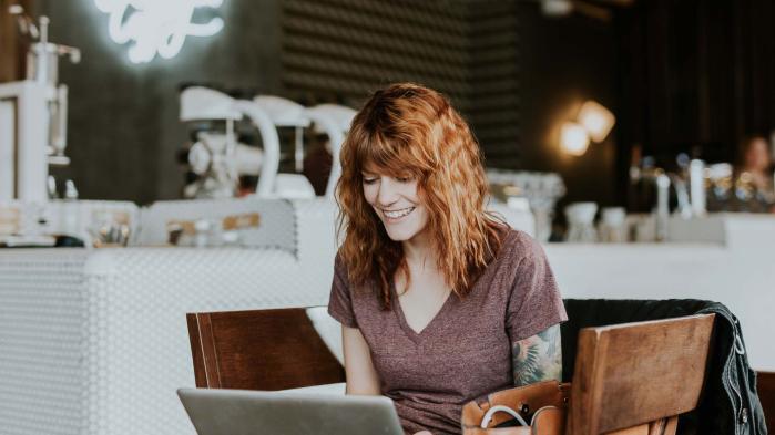 Frau mit roten Haaren sitzt an einem Tisch und arbeitet dank Desktop Virtualisierung mit ihrem Laptop im Cafe