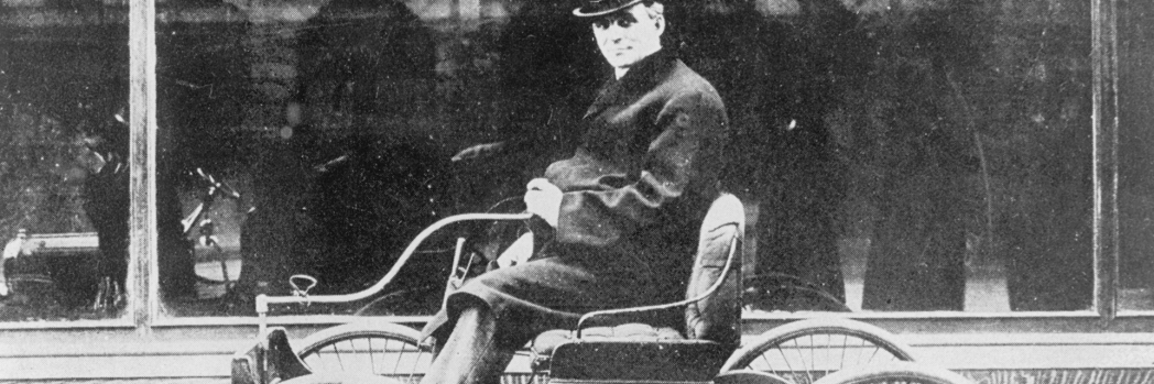 Schwarz-weiß-Foto von Henry Ford auf einem historischen Automodel