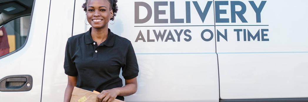A woman stands in front of a white van with a parcel.