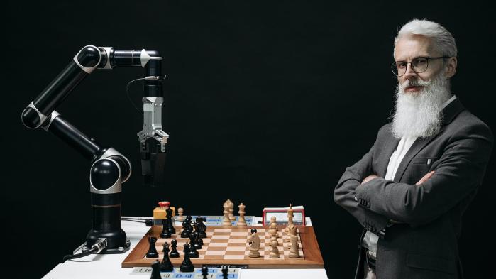 Older man with gray hair stands in a laboratory and plays chess against artificial intelligence