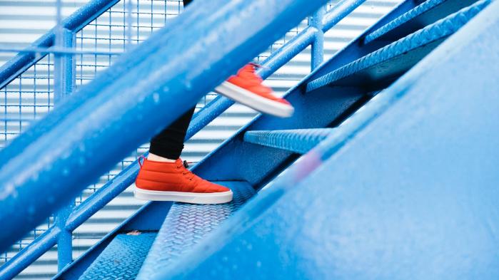 Person mit roten Schuhen läuft eine blaue Treppe in einer Lagerhalle hoch