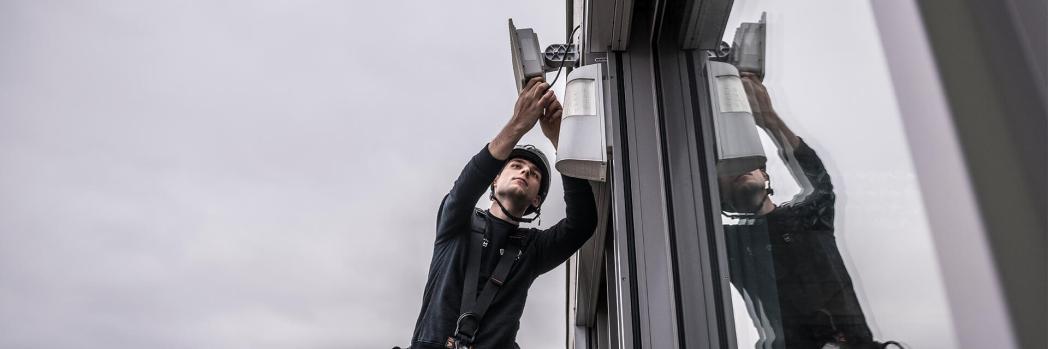 Techniker installiert an Außenfassade einer Logistikhalle WLAN-Komponenten