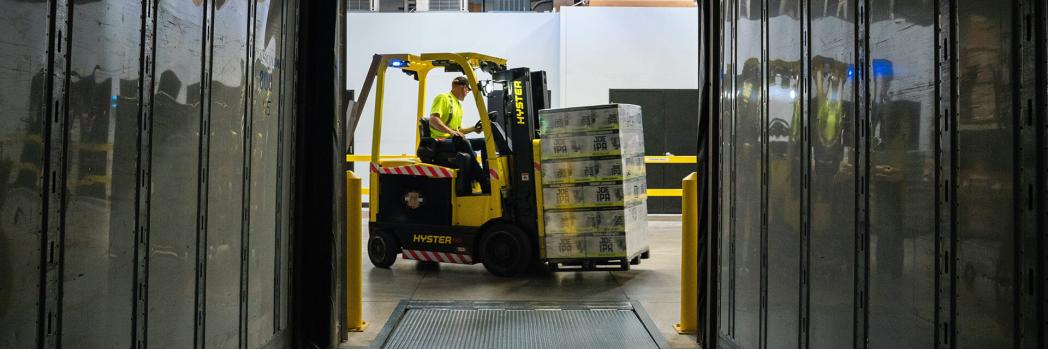 Employee drives through warehouse with loaded forklift, representing warehouse management systems and lower logistics costs