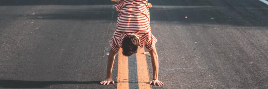 Man in red and white striped T-shirt and black trousers makes a handstand in the middle of the street
