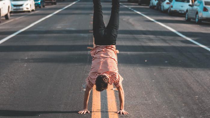 Man in red and white striped T-shirt and black trousers makes a handstand in the middle of the street