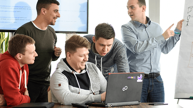 Eine Gruppe Mitarbeiter unterhält sich, während 3 Mitarbeiter auf einen Laptop schauen.