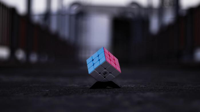 Rubik's cube with blue, pink and white side lies on a dark road