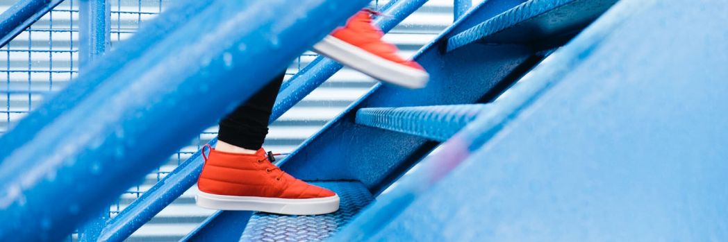 Three tips for a new TMS: new processes, microservices for subtasks, and an open system with API. Person with red shoes walks up blue stairs in warehouse